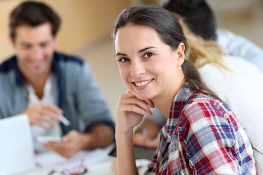 Gruppe Student*innen am Tisch, im Vordergrund junge Frau mit Blick zur/m Betrachter*in