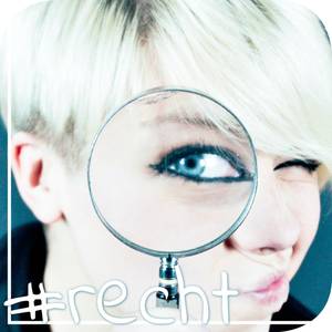 Junge Frau mit kurzen blonden Haaren schaut durch eine große Lupe auf die/den Betrachter*in.