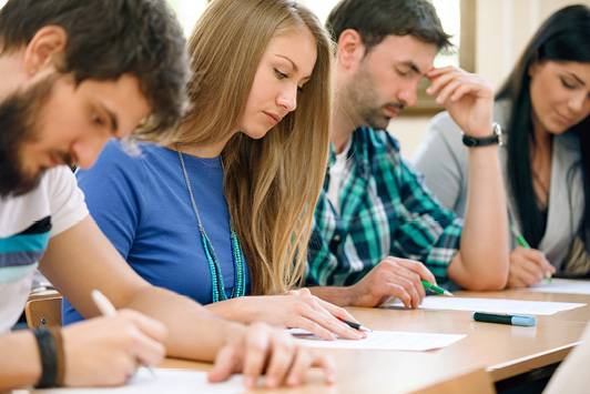 Eine Studentin sitzt zwischen drei Studierenden: Alle konzentrieren sich auf vor sich liegende Dokumente.